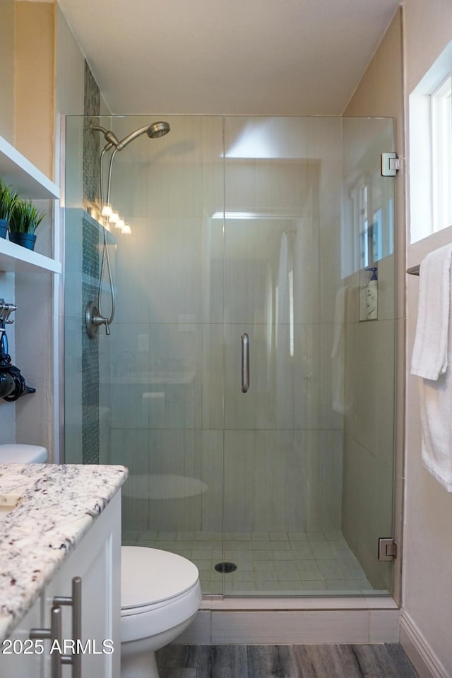 bathroom with toilet, hardwood / wood-style flooring, a shower with shower door, and vanity