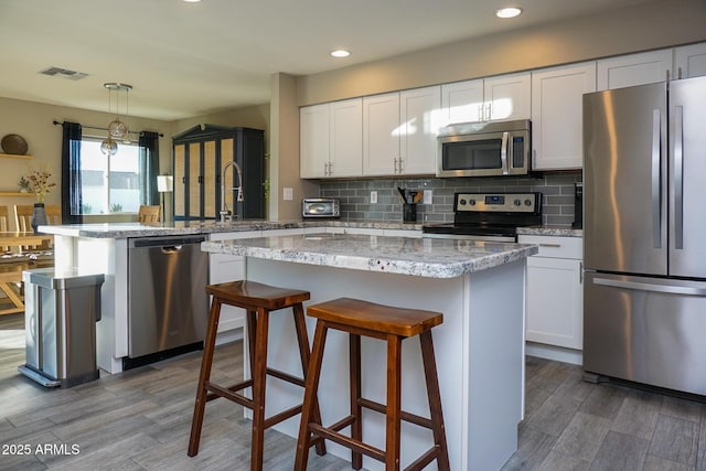 kitchen featuring stainless steel appliances, white cabinets, decorative backsplash, hanging light fixtures, and a kitchen island