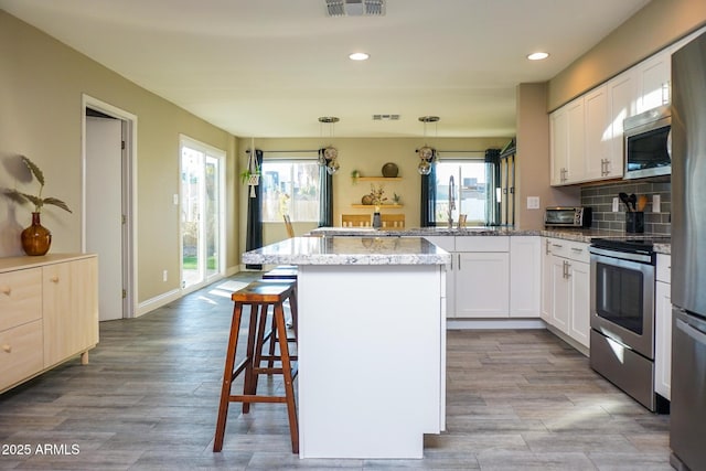 kitchen featuring backsplash, stainless steel appliances, white cabinets, and hanging light fixtures