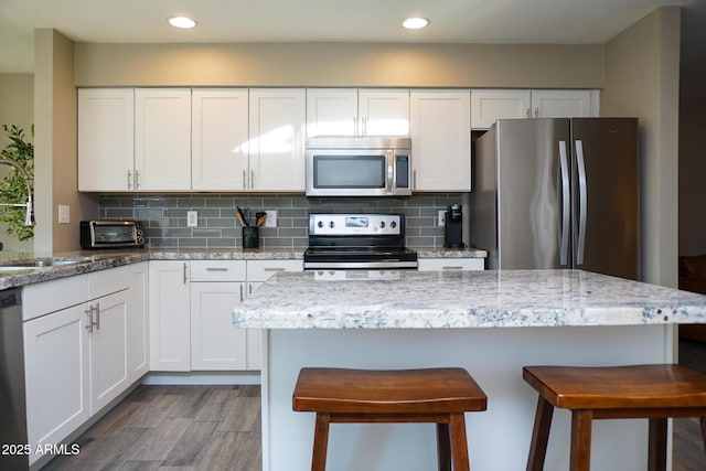 kitchen featuring stainless steel appliances, white cabinetry, backsplash, and light stone countertops