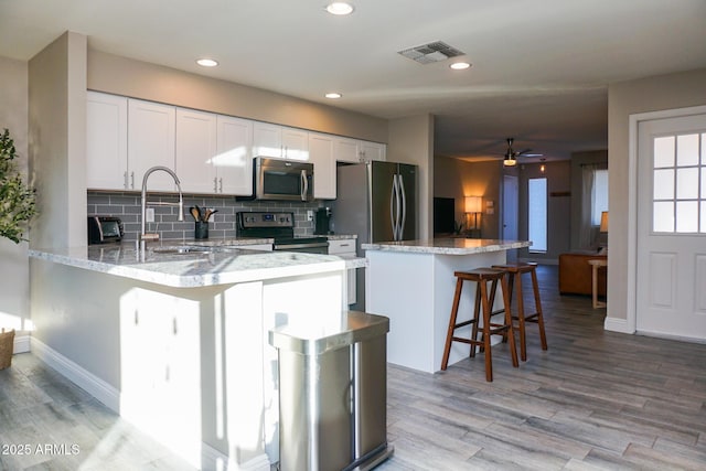 kitchen with stainless steel appliances, a breakfast bar, backsplash, white cabinetry, and sink