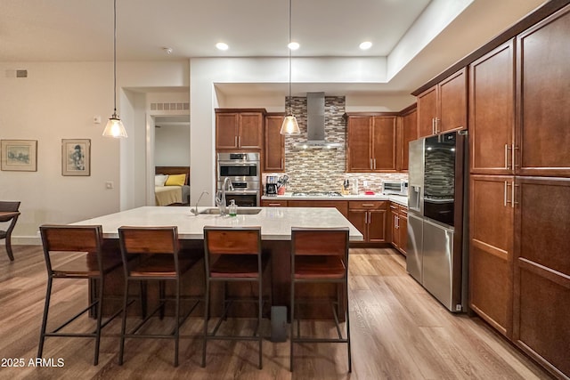 kitchen featuring appliances with stainless steel finishes, an island with sink, decorative backsplash, wall chimney exhaust hood, and decorative light fixtures