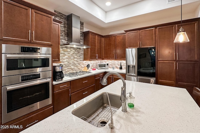 kitchen with appliances with stainless steel finishes, light stone countertops, decorative backsplash, wall chimney exhaust hood, and sink