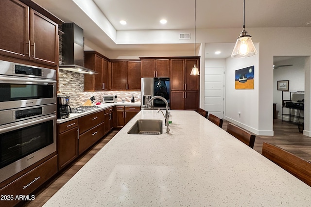 kitchen featuring stainless steel appliances, sink, wall chimney exhaust hood, light stone countertops, and pendant lighting