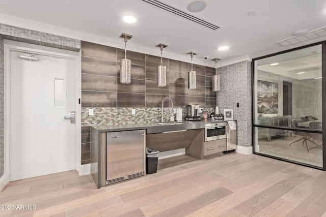 kitchen featuring stainless steel appliances, sink, light hardwood / wood-style flooring, decorative light fixtures, and backsplash