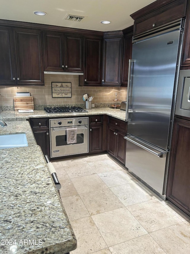 kitchen featuring backsplash, light stone counters, dark brown cabinetry, stainless steel appliances, and sink