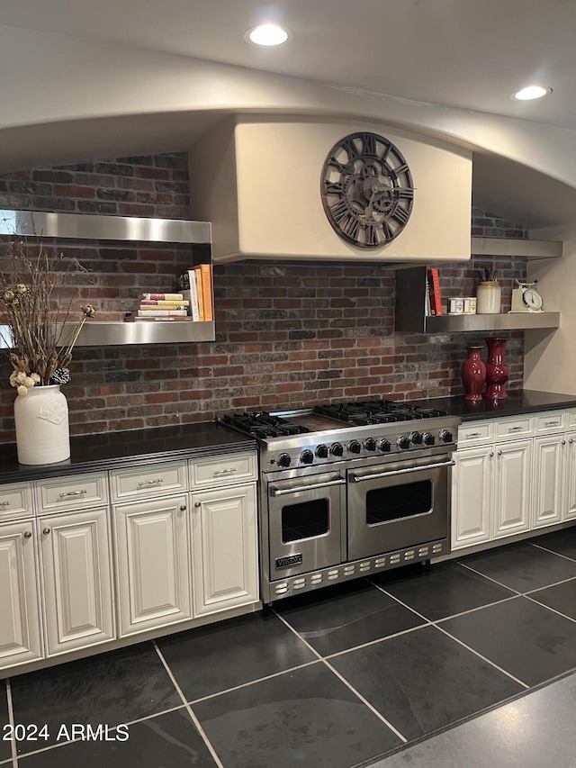 kitchen with dark tile patterned floors, double oven range, vaulted ceiling, white cabinets, and exhaust hood