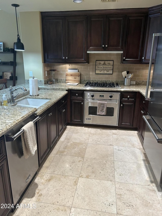 kitchen with backsplash, sink, light stone countertops, dark brown cabinetry, and stainless steel appliances