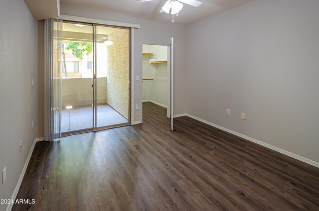 unfurnished bedroom featuring dark wood-type flooring, a closet, a walk in closet, and ceiling fan