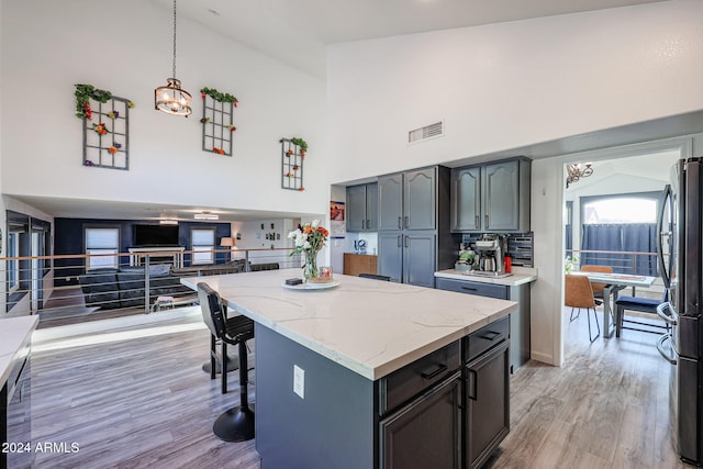 kitchen featuring a center island, high vaulted ceiling, hanging light fixtures, light hardwood / wood-style flooring, and stainless steel fridge