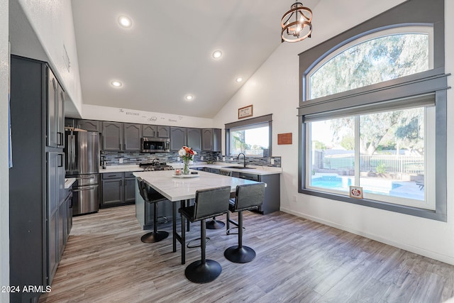 kitchen with high vaulted ceiling, decorative backsplash, light wood-type flooring, decorative light fixtures, and stainless steel appliances