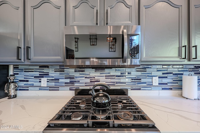 kitchen featuring backsplash, light stone counters, and gray cabinetry