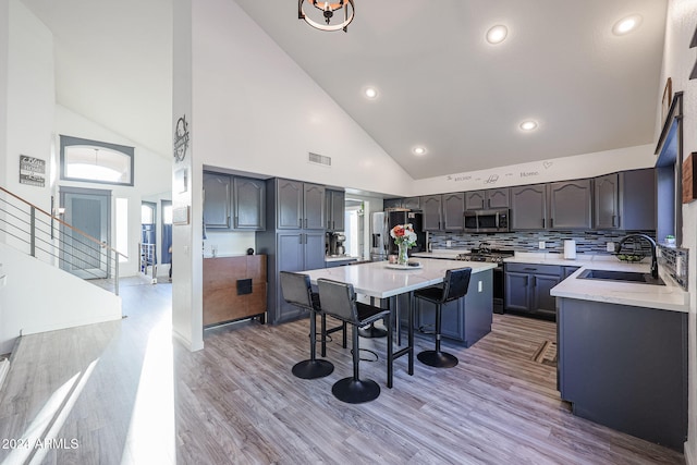 kitchen featuring a breakfast bar, high vaulted ceiling, sink, light hardwood / wood-style flooring, and stainless steel appliances