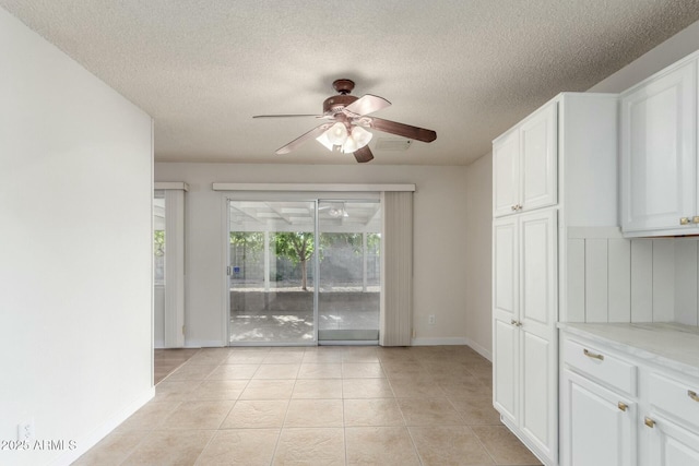interior space with light tile patterned floors, a textured ceiling, baseboards, and ceiling fan