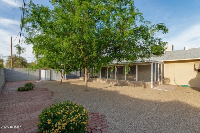 view of yard featuring a sunroom, an outbuilding, a fenced backyard, and a patio area
