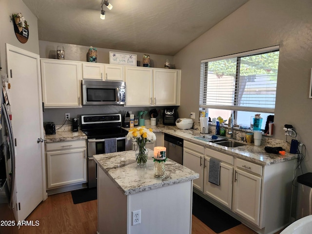 kitchen featuring appliances with stainless steel finishes, a sink, vaulted ceiling, wood finished floors, and white cabinets