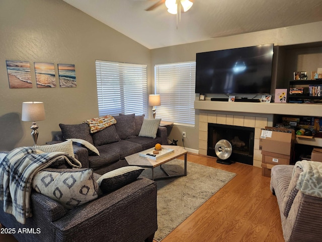 living room featuring vaulted ceiling, ceiling fan, wood finished floors, and a tile fireplace