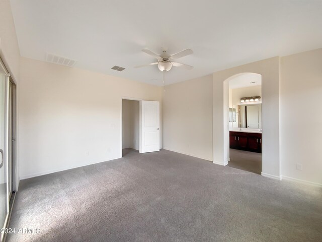 unfurnished bedroom featuring visible vents, arched walkways, and carpet flooring