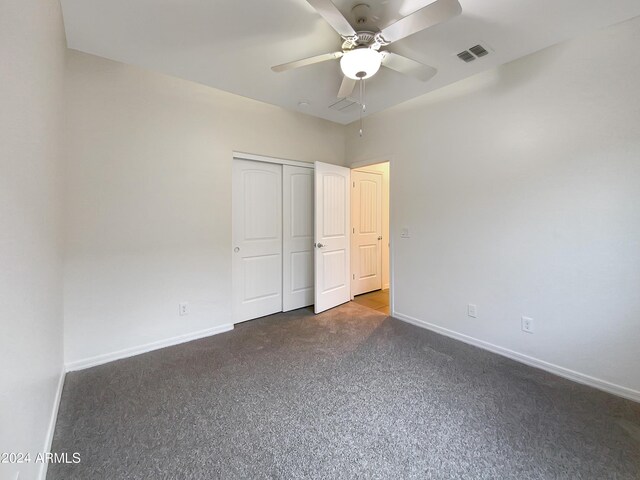 unfurnished bedroom featuring baseboards, visible vents, ceiling fan, dark carpet, and a closet