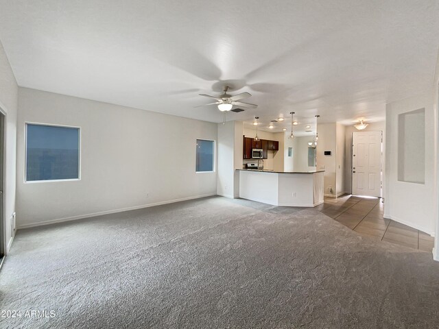 unfurnished living room featuring dark tile patterned floors, baseboards, dark colored carpet, and a ceiling fan