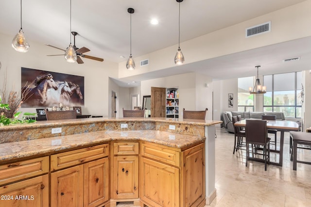 kitchen featuring pendant lighting, light stone counters, and ceiling fan with notable chandelier