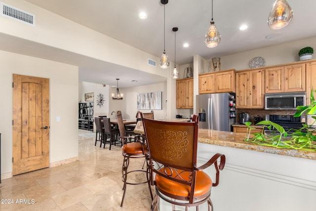 kitchen featuring light stone countertops, decorative light fixtures, light brown cabinetry, backsplash, and appliances with stainless steel finishes