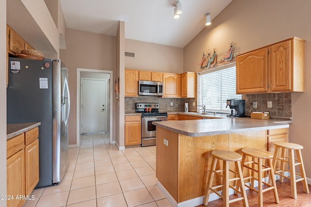 kitchen featuring light tile patterned floors, appliances with stainless steel finishes, a kitchen breakfast bar, backsplash, and kitchen peninsula