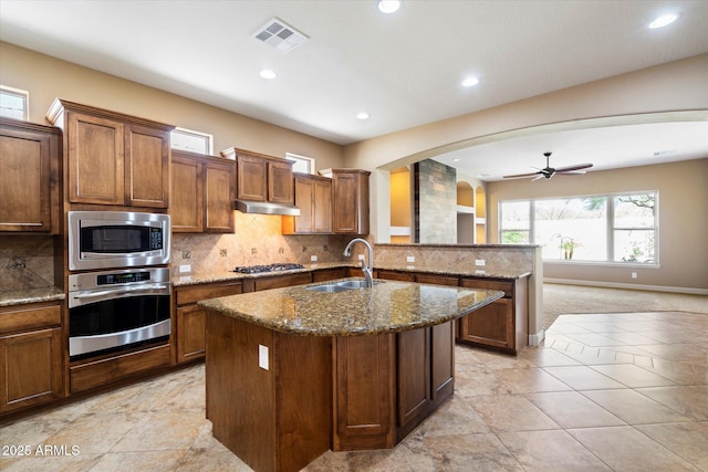 kitchen with visible vents, arched walkways, a sink, stainless steel appliances, and under cabinet range hood