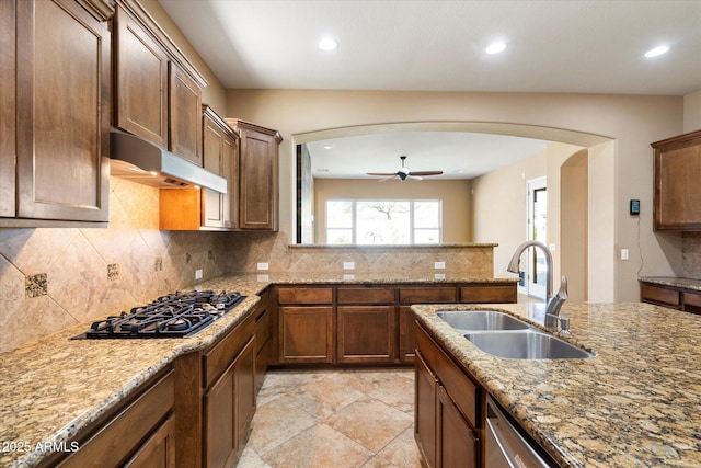 kitchen featuring backsplash, under cabinet range hood, appliances with stainless steel finishes, arched walkways, and a sink