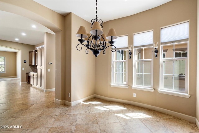 unfurnished dining area featuring recessed lighting, baseboards, a notable chandelier, and arched walkways