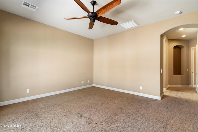 carpeted empty room with ceiling fan, visible vents, arched walkways, and baseboards