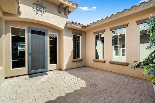 view of exterior entry featuring a tiled roof, a patio area, and stucco siding