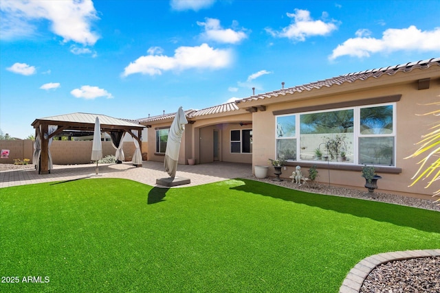 rear view of property featuring stucco siding, a tile roof, a patio, fence, and a gazebo