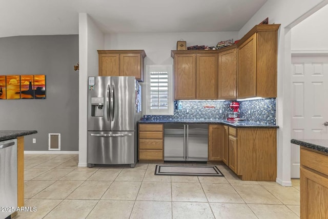 kitchen with light tile patterned floors, brown cabinetry, stainless steel appliances, baseboards, and backsplash