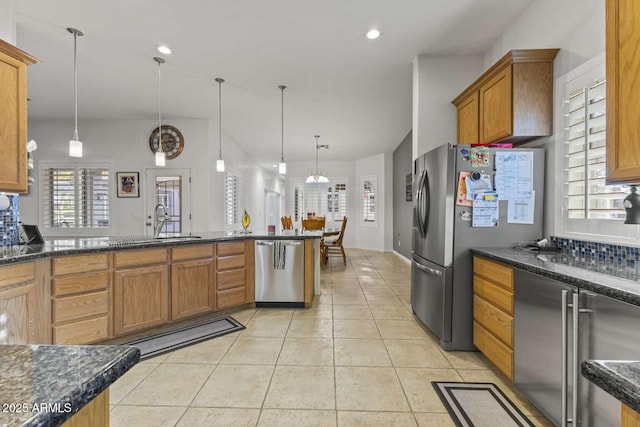 kitchen featuring brown cabinetry, appliances with stainless steel finishes, light tile patterned flooring, a sink, and decorative light fixtures