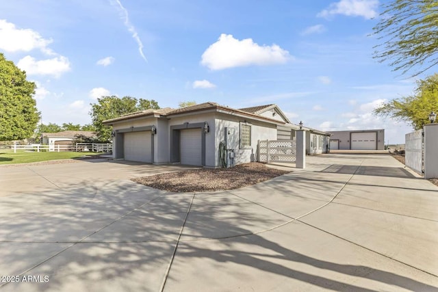 view of side of property featuring stucco siding, fence, a tile roof, an attached garage, and driveway