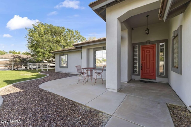 property entrance with a patio, stucco siding, and fence