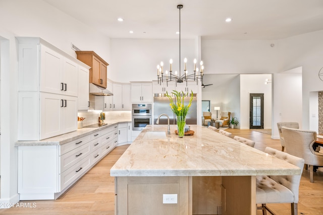 kitchen featuring a large island with sink, sink, stainless steel double oven, white cabinets, and light hardwood / wood-style flooring