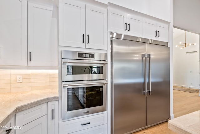 kitchen featuring tasteful backsplash, hanging light fixtures, light hardwood / wood-style floors, stainless steel appliances, and white cabinets