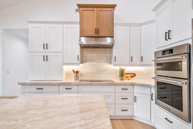 kitchen featuring white cabinetry, black electric cooktop, range hood, light stone counters, and stainless steel double oven