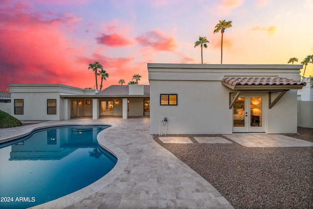 pool at dusk featuring french doors and a patio