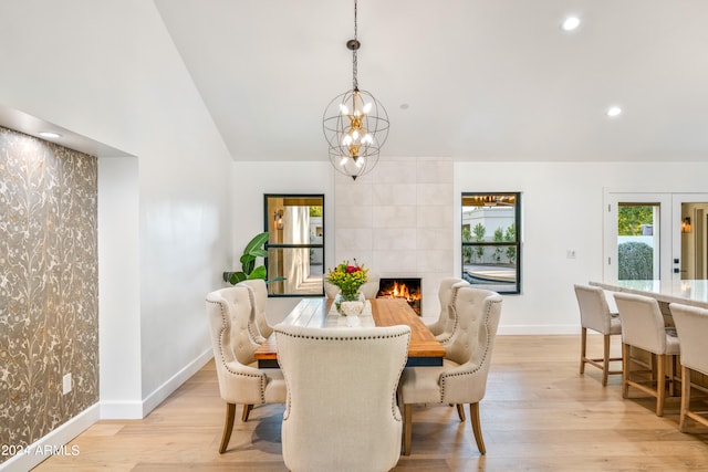 dining space with an inviting chandelier, vaulted ceiling, a fireplace, and light hardwood / wood-style floors