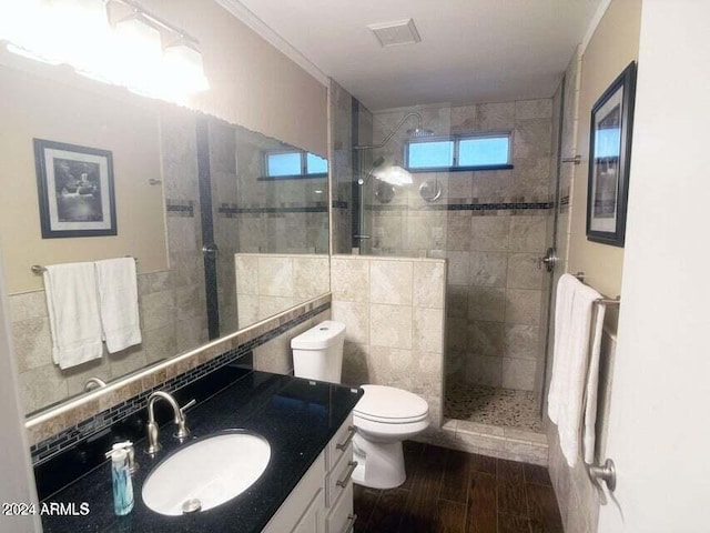 bathroom with toilet, tiled shower, vanity, tile walls, and hardwood / wood-style flooring