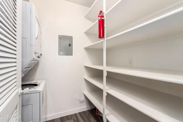 storage area featuring electric panel and stacked washing maching and dryer