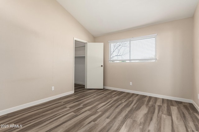 unfurnished bedroom with lofted ceiling, a closet, wood finished floors, and baseboards