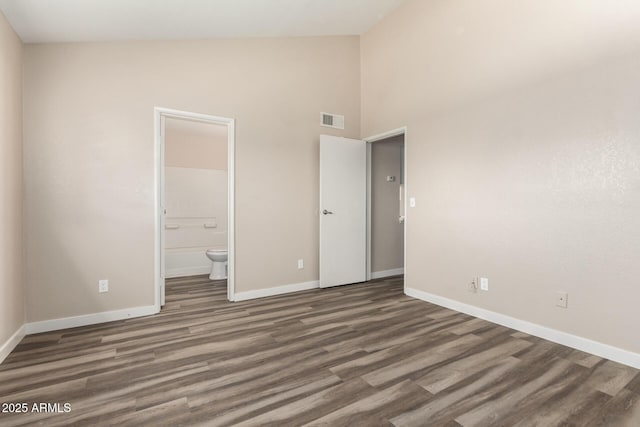 unfurnished bedroom with baseboards, visible vents, connected bathroom, wood finished floors, and high vaulted ceiling