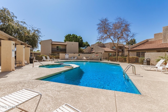 community pool with a patio, fence, a residential view, and a hot tub