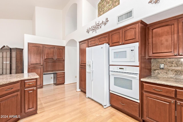 kitchen featuring light stone counters, white appliances, a towering ceiling, and tasteful backsplash