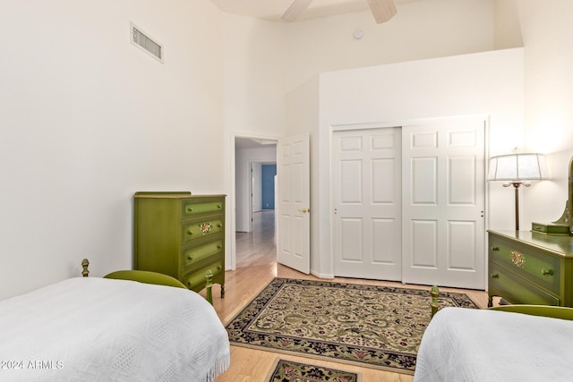 bedroom featuring ceiling fan, wood-type flooring, a high ceiling, and a closet