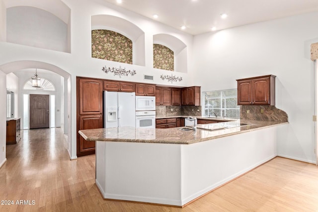 kitchen with light stone counters, kitchen peninsula, a towering ceiling, white appliances, and decorative backsplash